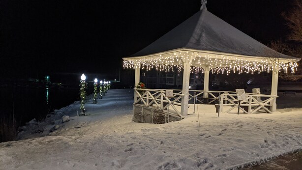A gazebo with a snow-covered ground, a bench, and a railing.
