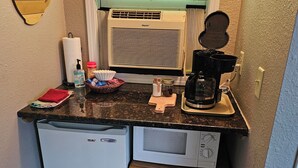 A compact kitchen with a refrigerator, microwave, coffee maker, and a small cabinet.