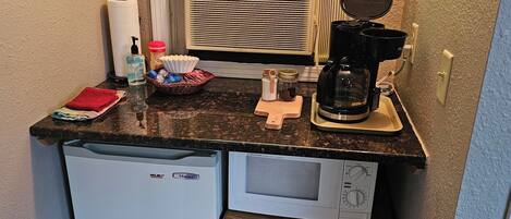 Una cucina compatta con frigorifero, microonde, macchina del caffè e un piccolo armadietto.