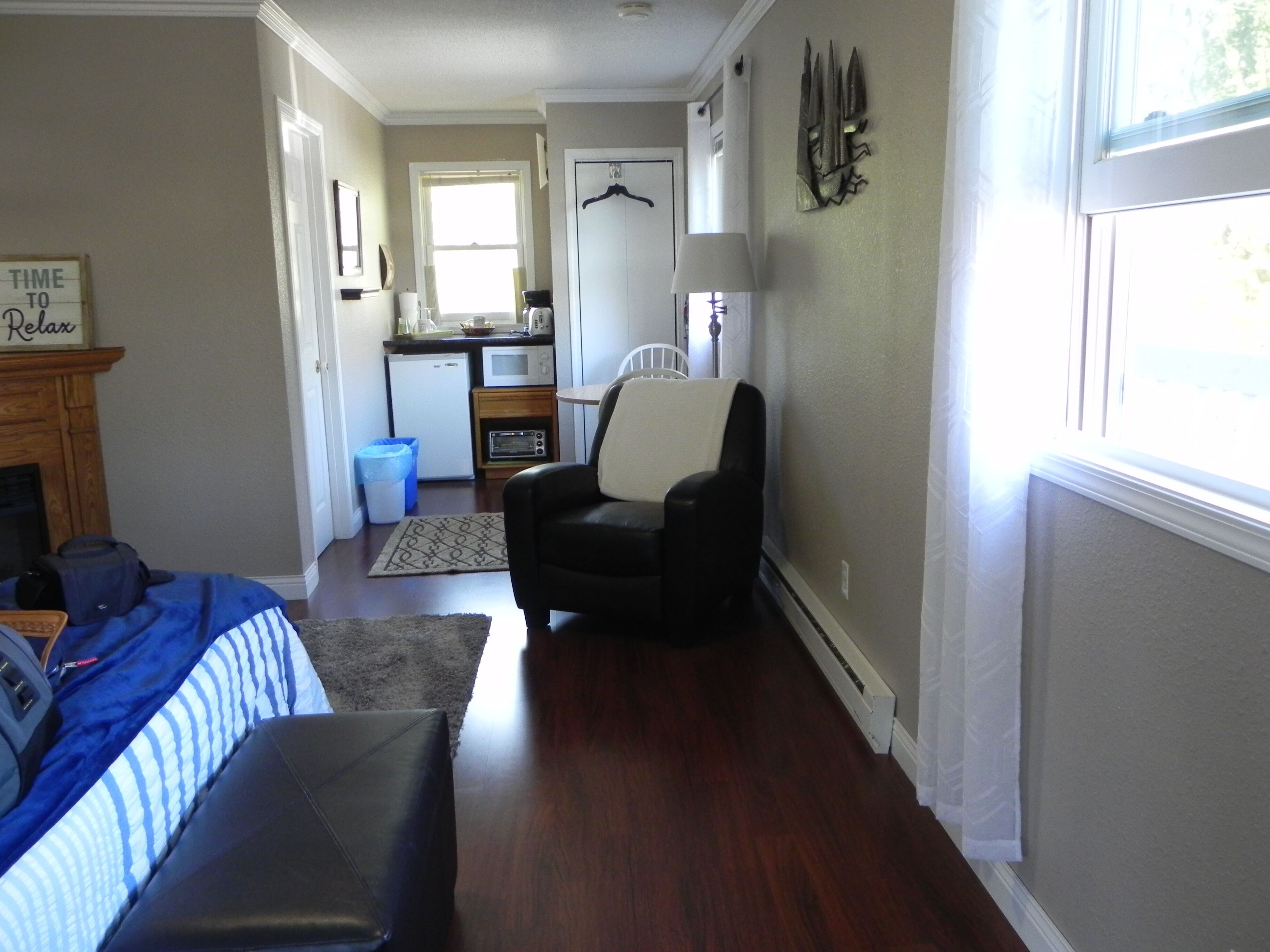 A compact living space with a kitchenette, a black leather chair, a bed with a blue and white striped blanket, and a fireplace.