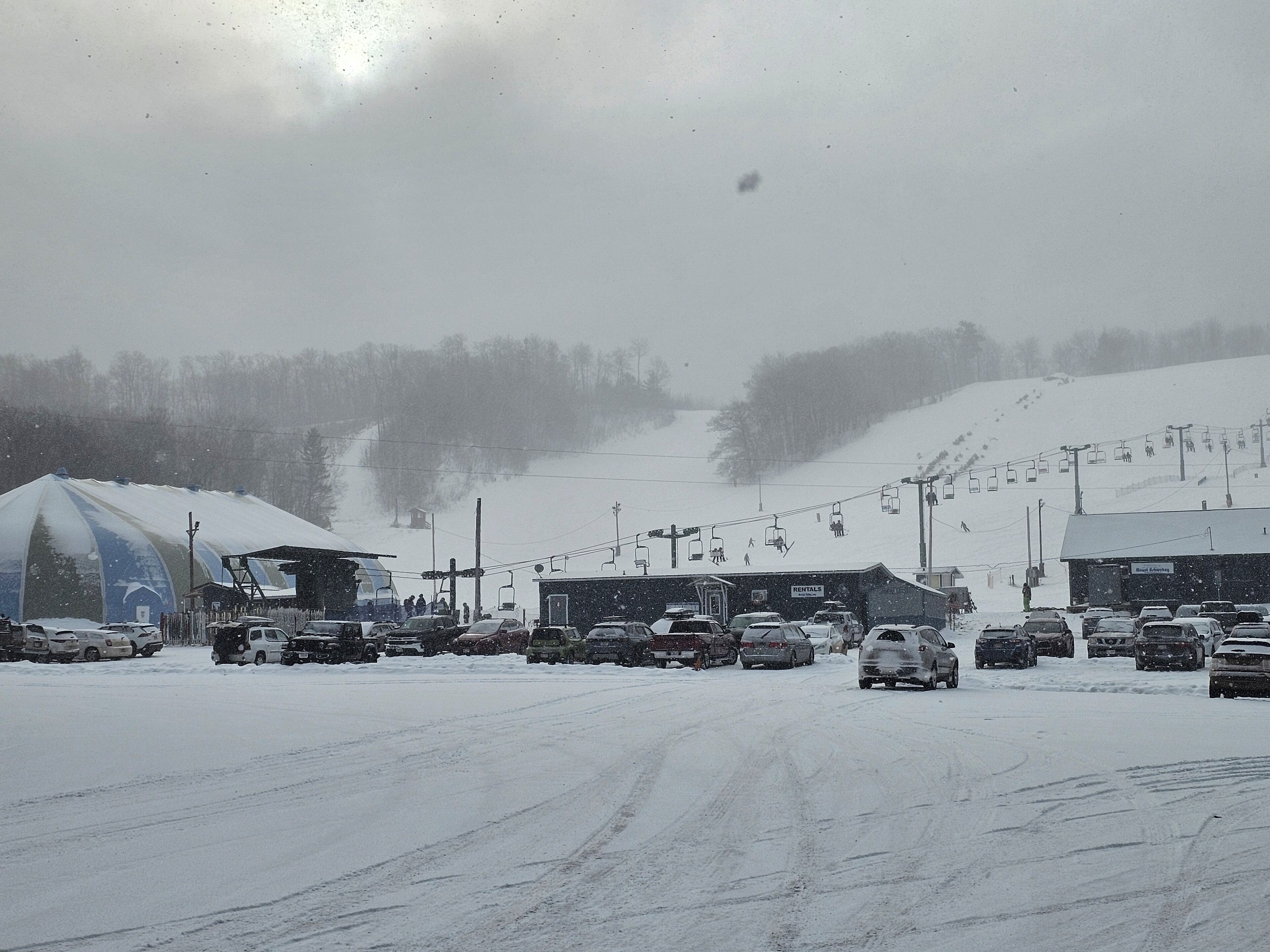 A snowy parking lot with cars and a ski lift in the background.