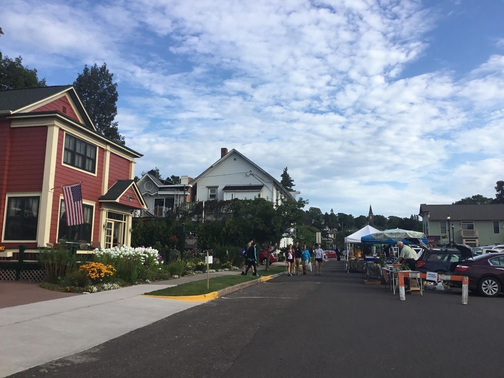 A street with houses, a sidewalk, and a market area with tents and people.
