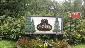 A welcome sign for Brookside Hide-A-Way with a stone border and a street sign indicating the address 34300 Port Superior Rd.