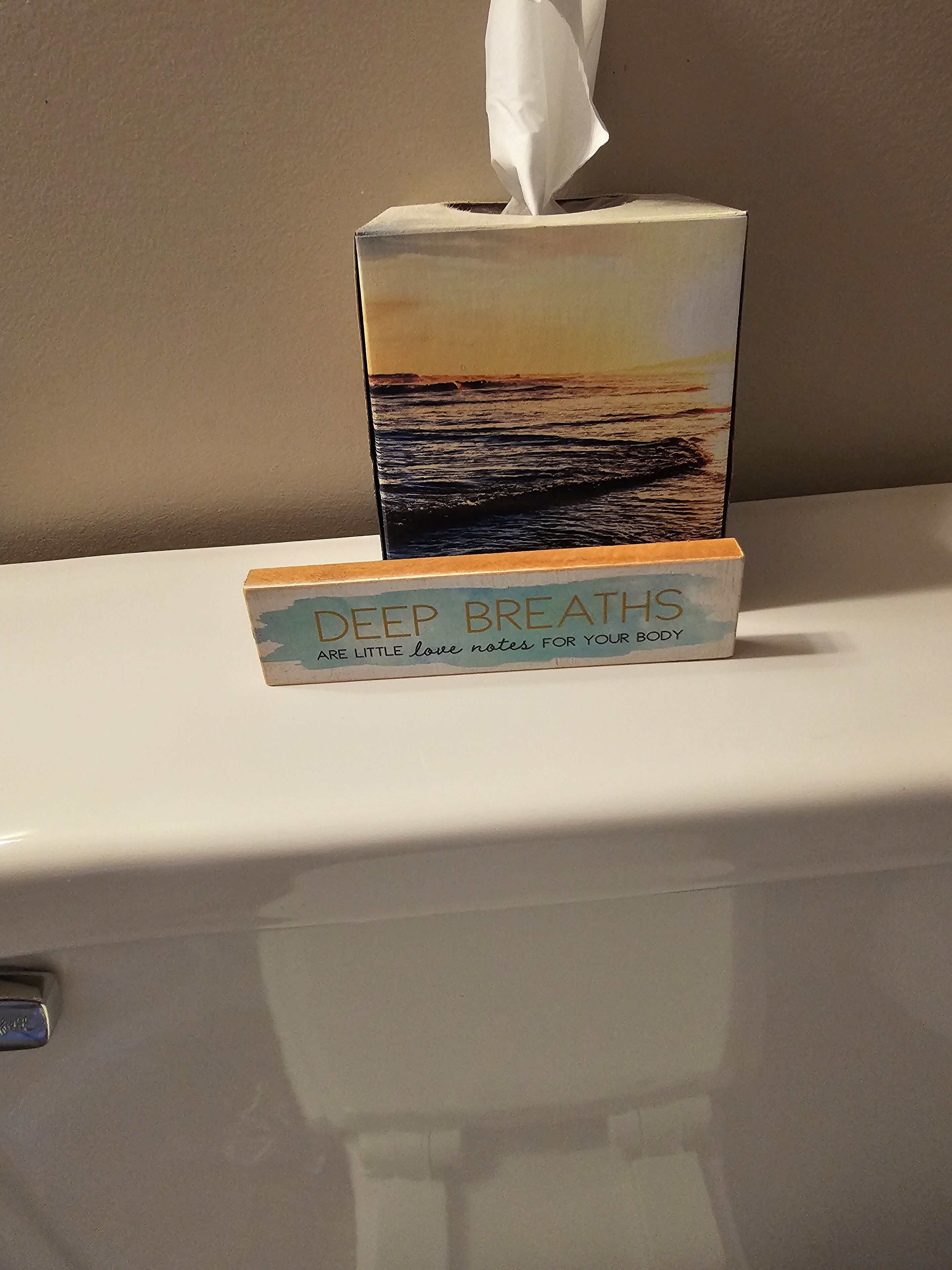 A tissue box with a sunset image and the text "DEEP BREATHS" on a white surface.