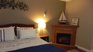 A neatly made bed with striped bedding, a bedside lamp, a fireplace with a sign above it, and a decorative wall piece.
