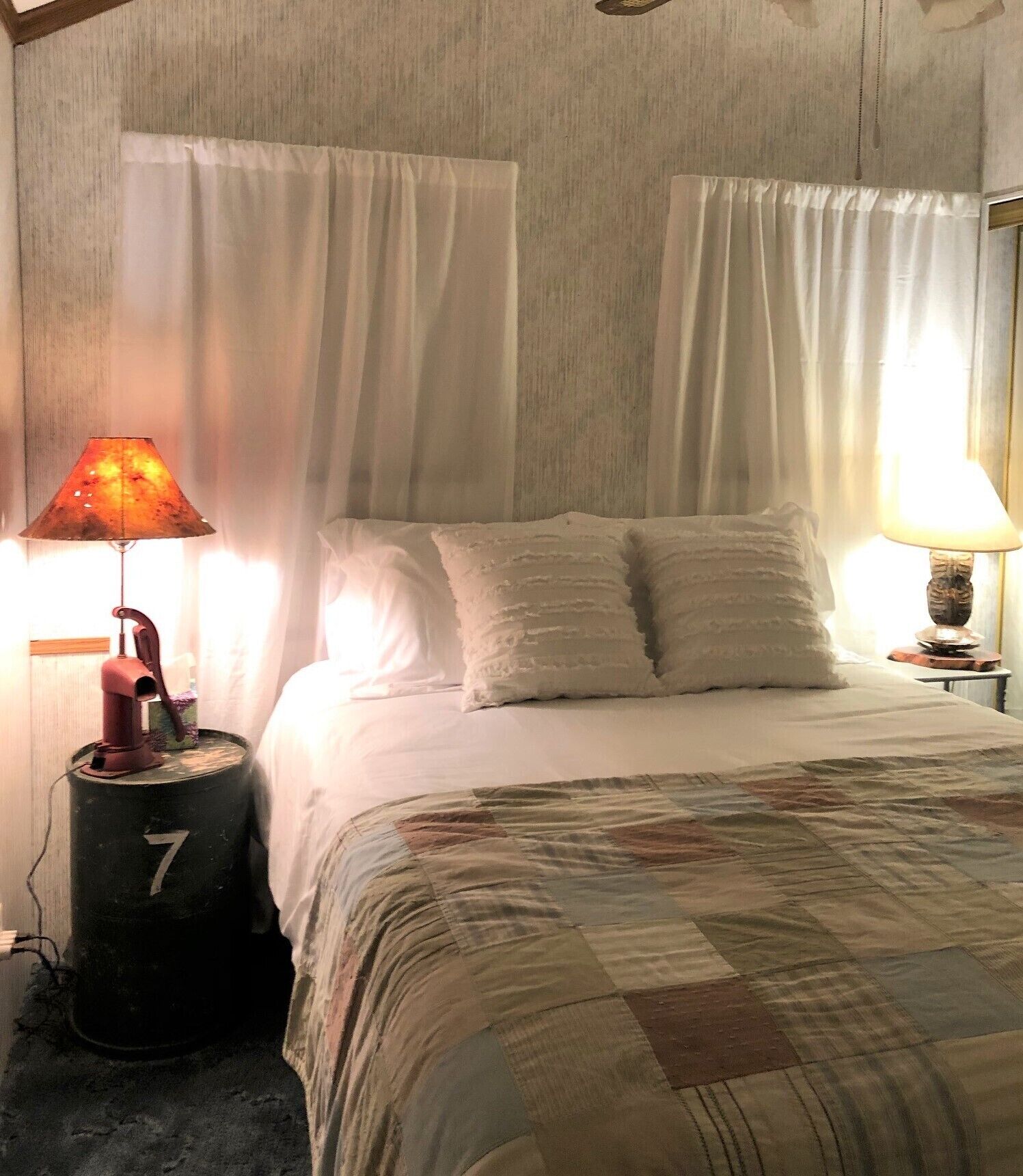 A bedroom with a bed, two bedside lamps, and a black barrel with the number 7 on it.