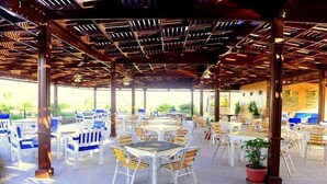 Un espace extérieur aménagé en terrasse, avec plusieurs tables et chaises, une structure de plafond en bois et des plantes en pot.
