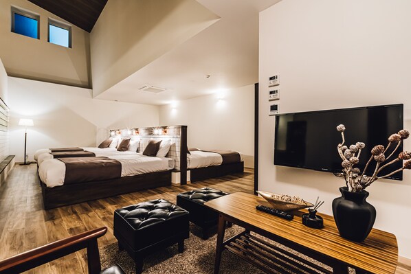 A modern hotel room with a loft bed, a flat-screen TV, a wooden desk, and a vase with dried flowers.