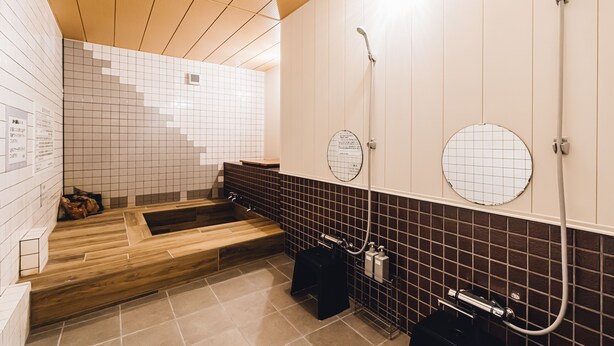 A modern bathroom with a wooden bench, a shower area, and a tiled wall with a grid pattern. - Yamahana Onsen Tondenyu Ryokan (Sapporo)