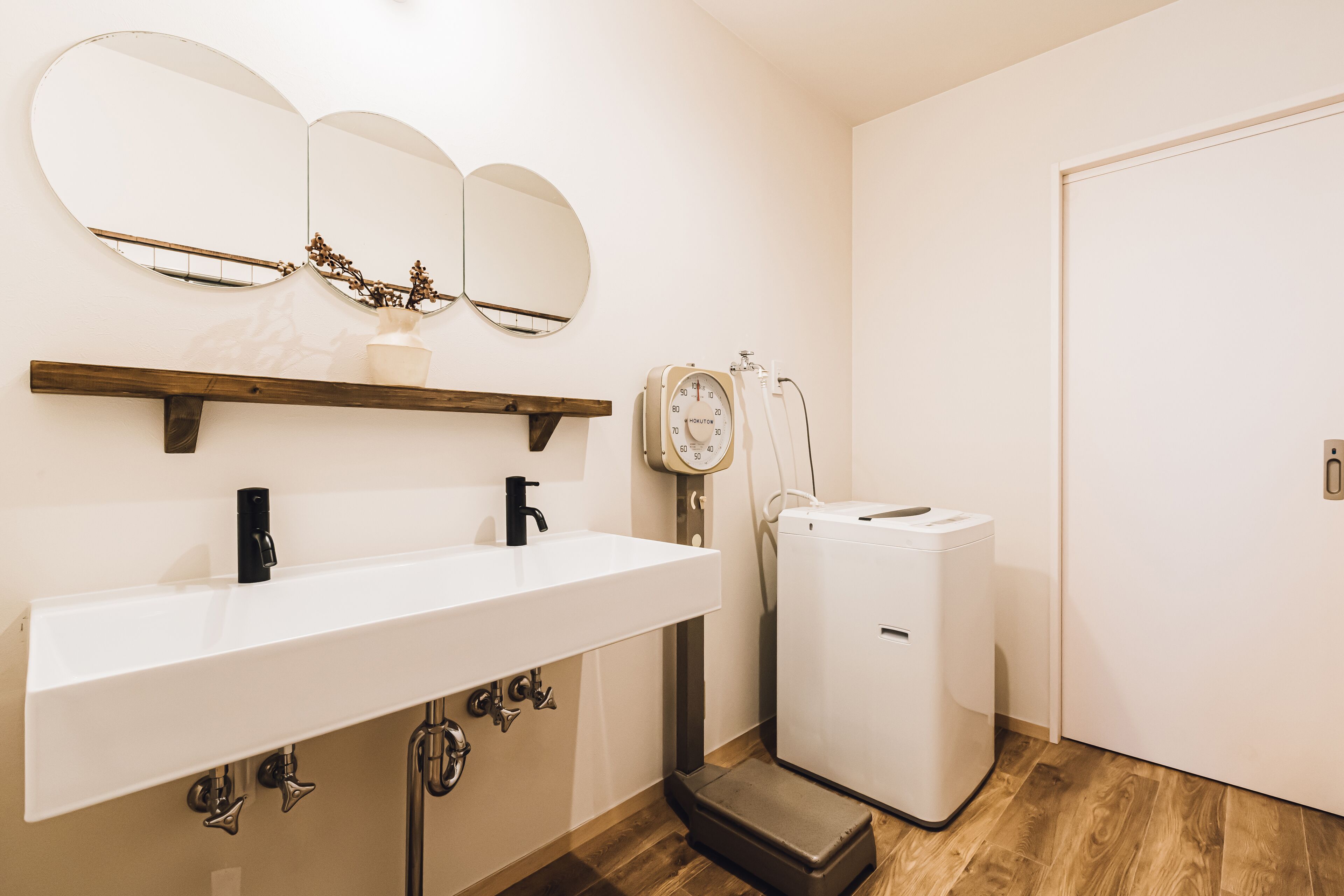 A bathroom with a white sink, two mirrors, a scale, and a compact white washing machine.