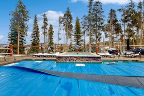 Relax by the pool surrounded by tall pine trees and lounge chairs.