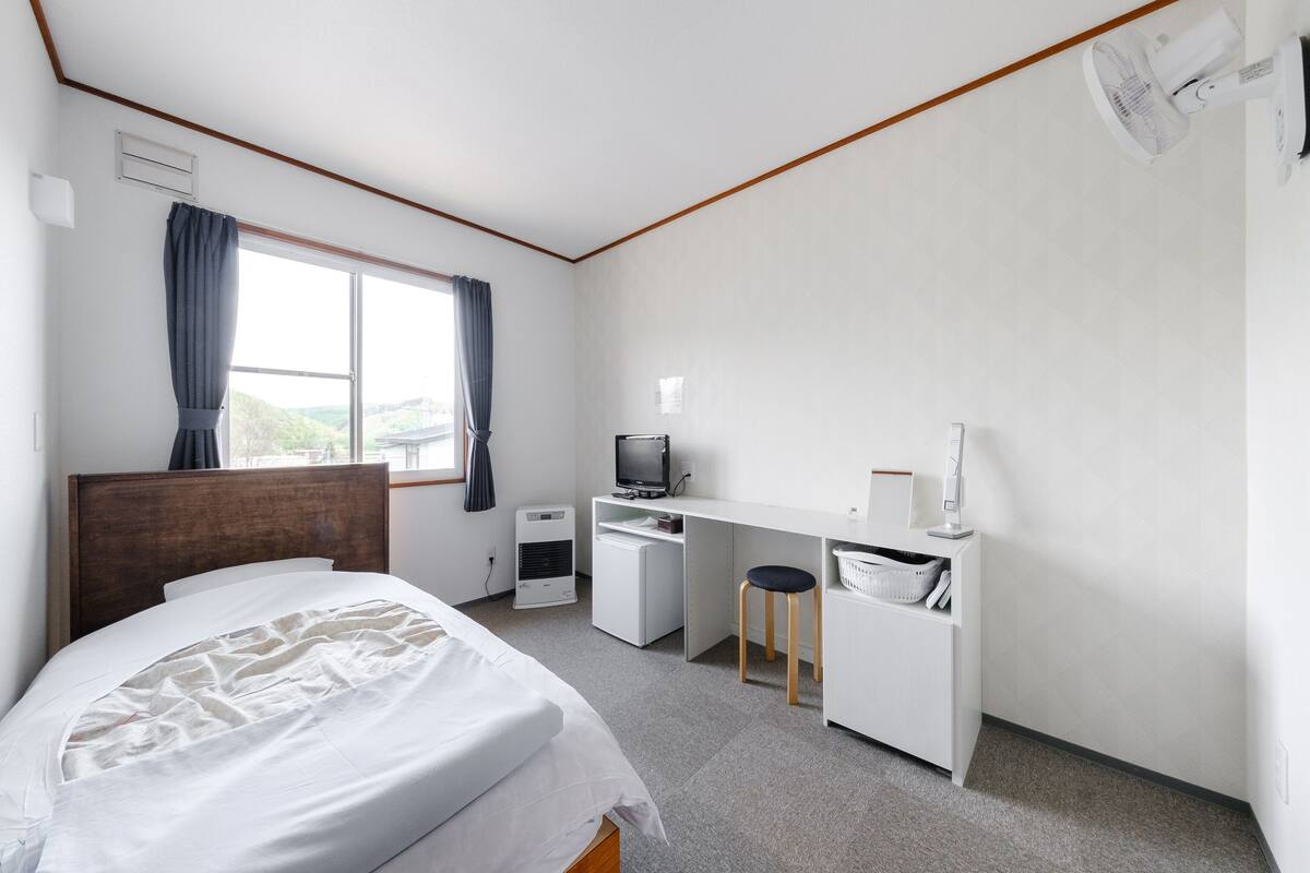Une chambre d’hôtel équipée d’un lit, d’un bureau, d’une chaise, d’une télévision et d’une fenêtre avec des rideaux.
