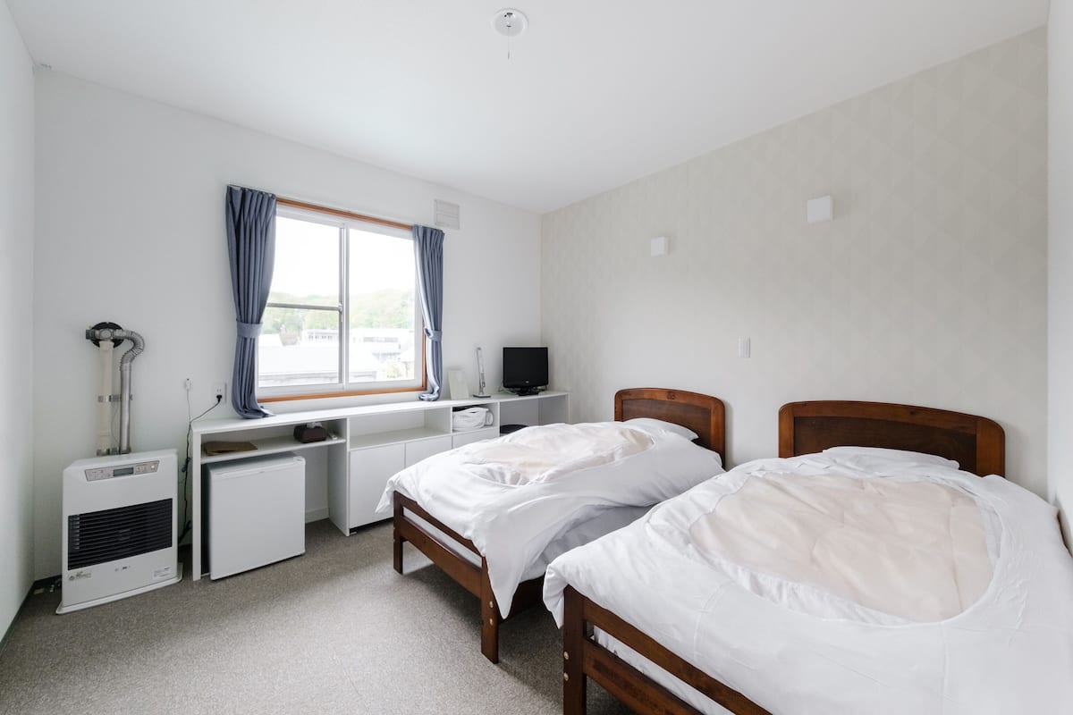 Une chambre avec deux lits simples, un bureau avec un ordinateur, un radiateur et une fenêtre avec des rideaux.
