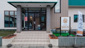 L’entrée de l’hôtel Shun, avec son panneau indicateur, ses marches et un espace verdoyant.
