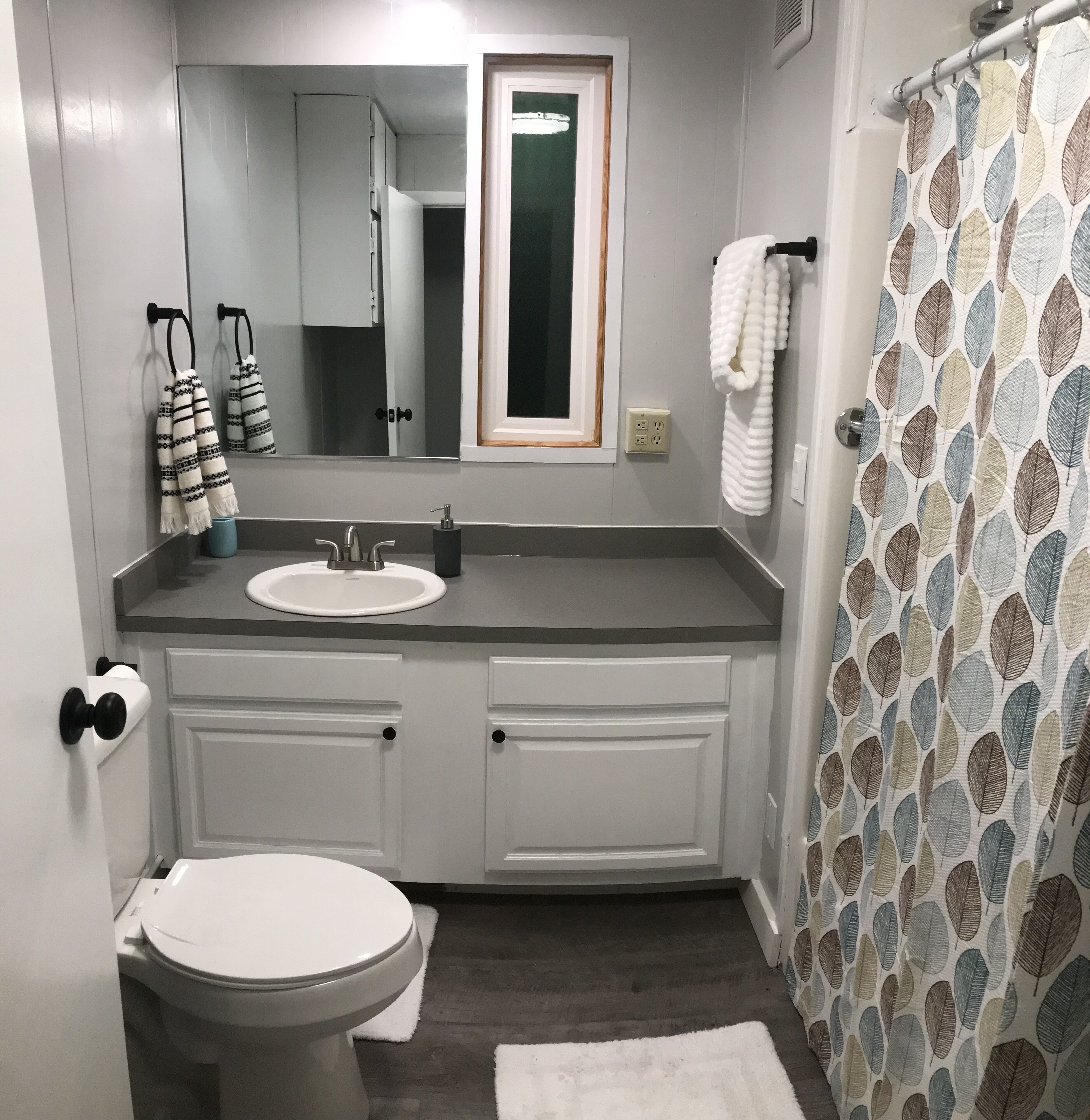 A bathroom with a white sink, a mirror above it, and a shower curtain with a leaf pattern.