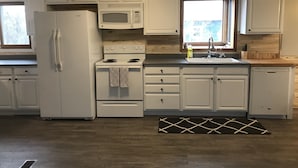 Una cocina con armarios blancos, un refrigerador, una estufa, un microondas, un lavamanos y un ventanal.