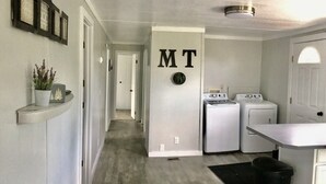 Un lavadero con lavadora y secadora, un cubo de basura y un cartel en la pared con las letras "MT".