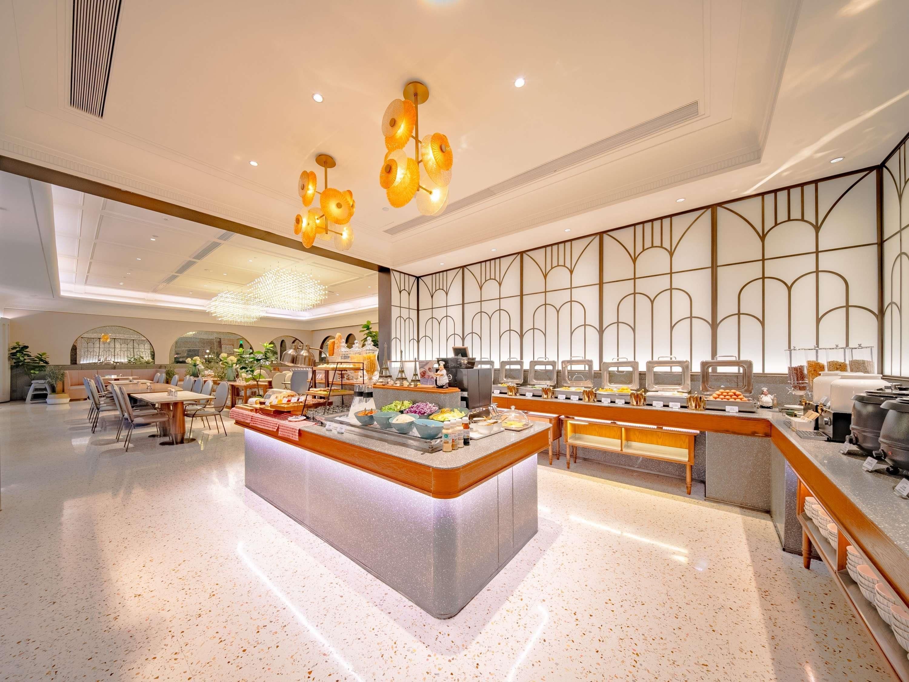 A modern hotel lobby with a central buffet area, seating arrangements, and decorative lighting.