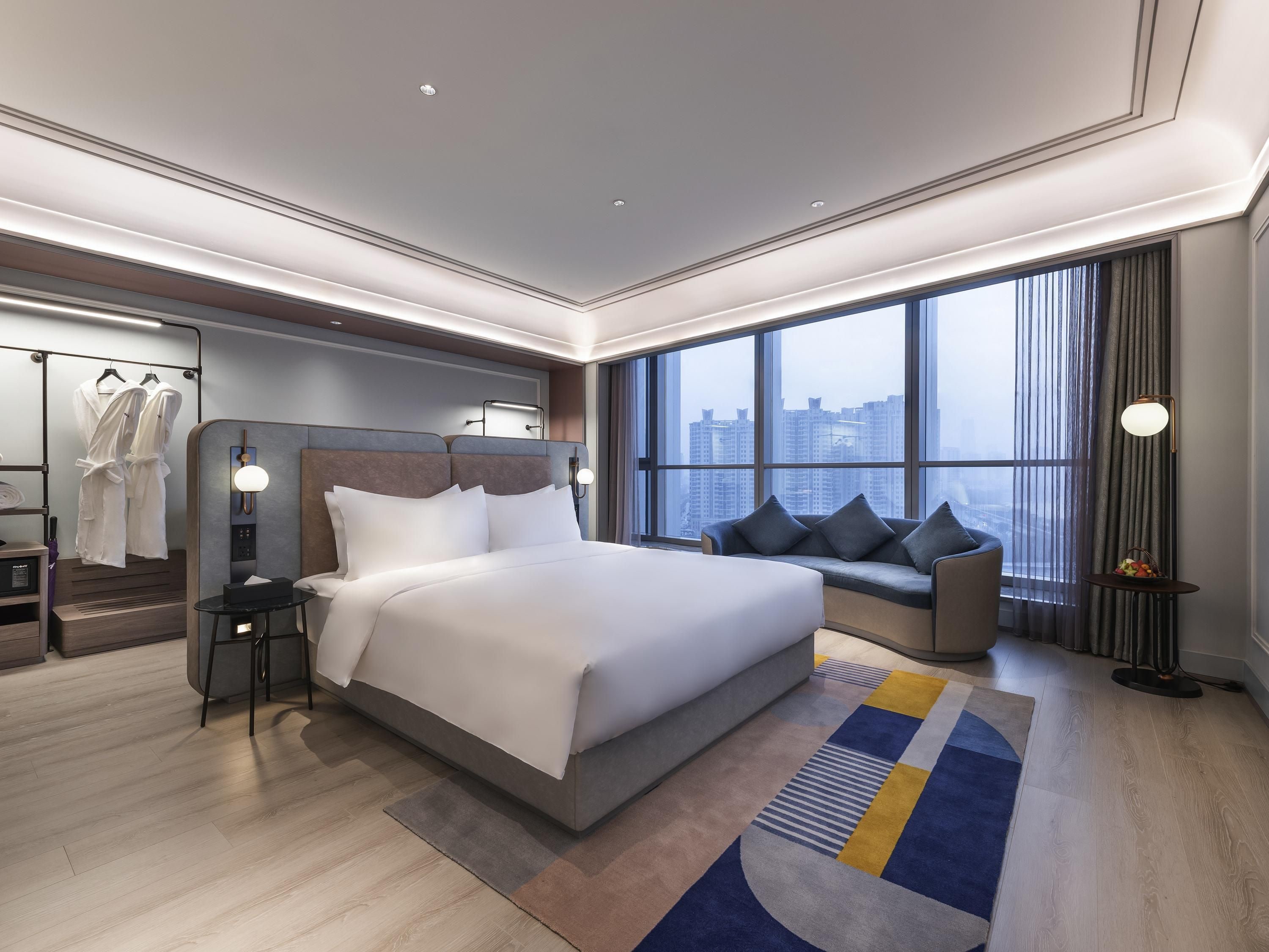 Une chambre d’hôtel moderne dotée d’un grand lit, d’un coin salon, d’une armoire et offrant une vue sur le paysage urbain.