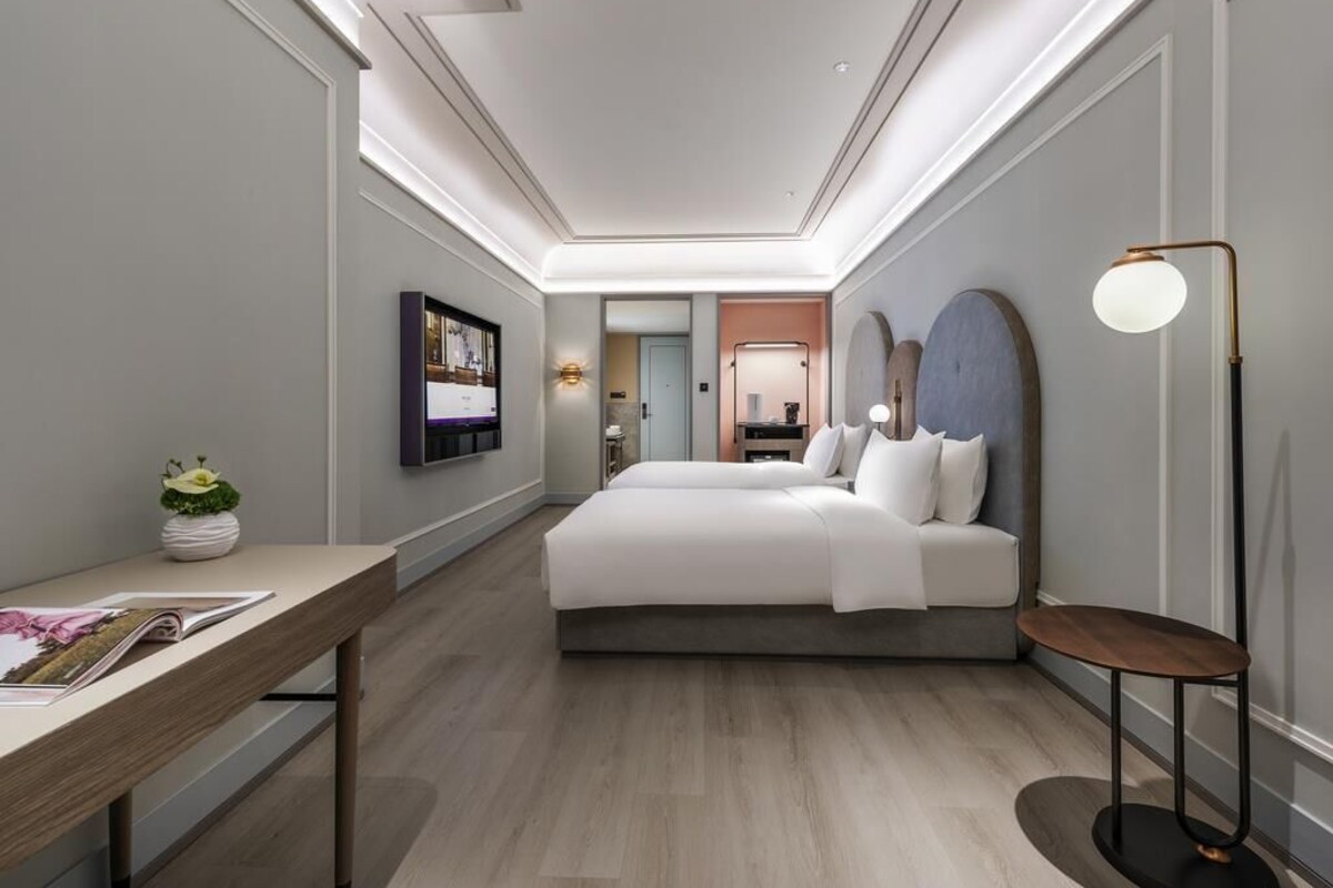 Una habitación de hotel moderna con una cama grande, un escritorio, un televisor de pantalla plana y una mesita de noche con una lámpara.