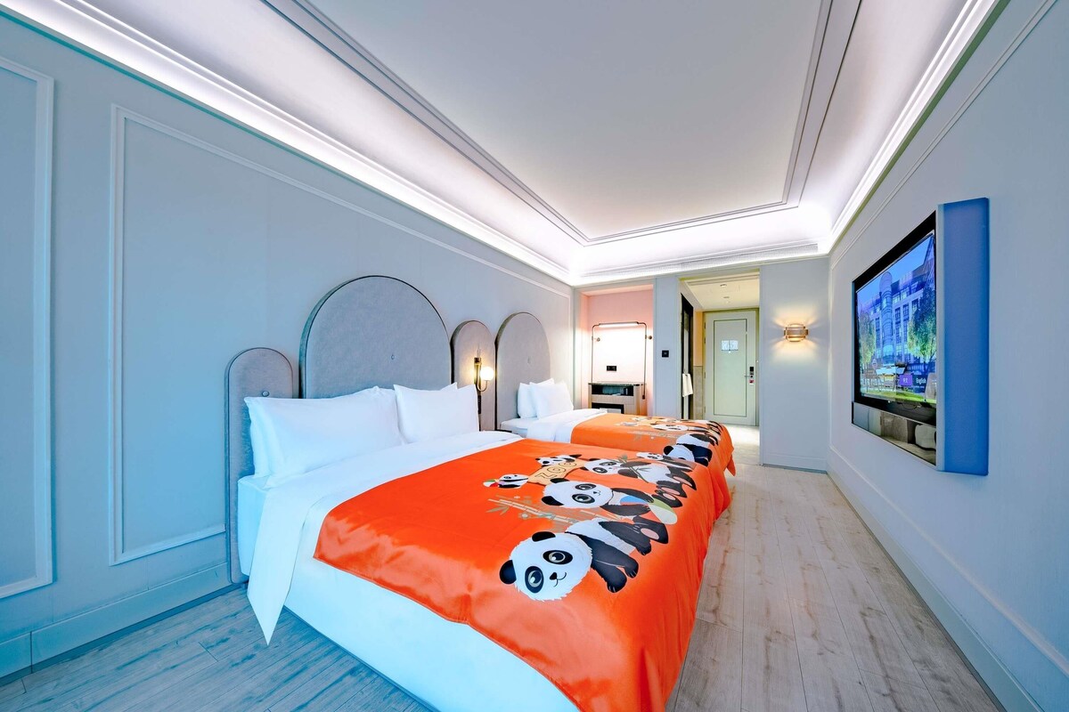 A hotel room with a large bed, a television on the wall, and a hallway leading to a bathroom.