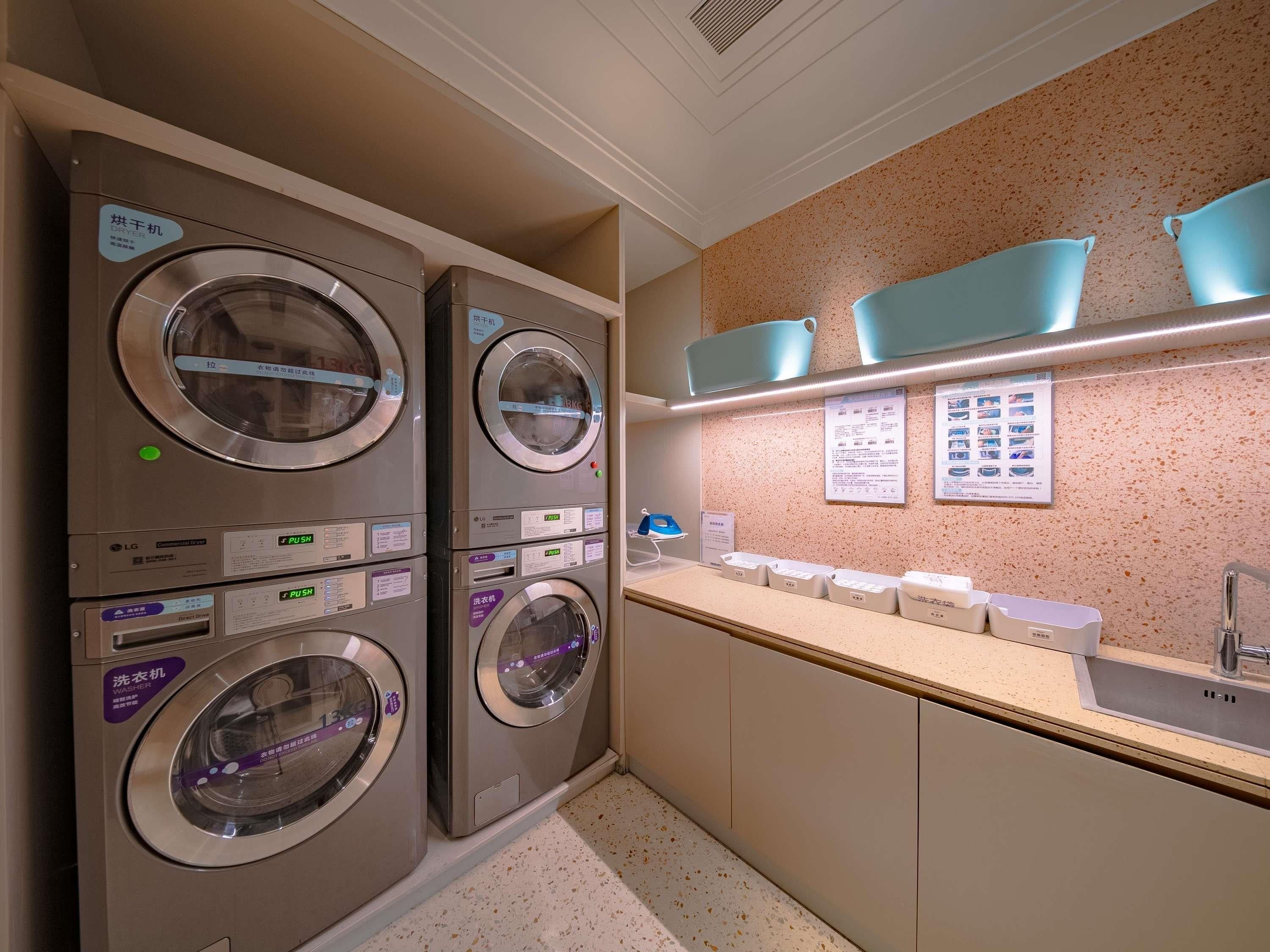 A laundry area with stacked washing machines and a sink with soap dispensers.