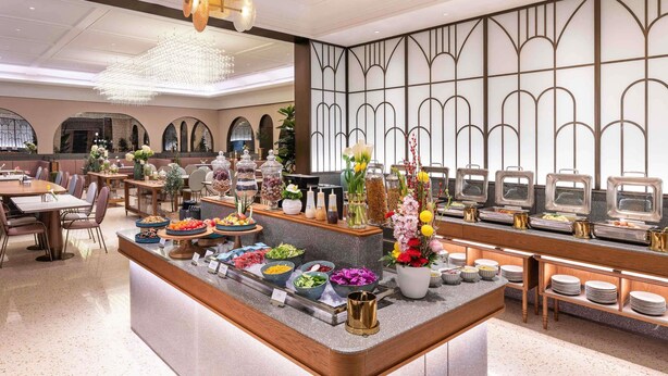 Un comedor de hotel moderno con barra de buffet, candelabros elegantes y una pared decorativa.