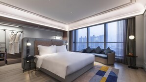 Una habitación de hotel moderna con una cama grande, una zona de estar, un armario y vistas a la ciudad.