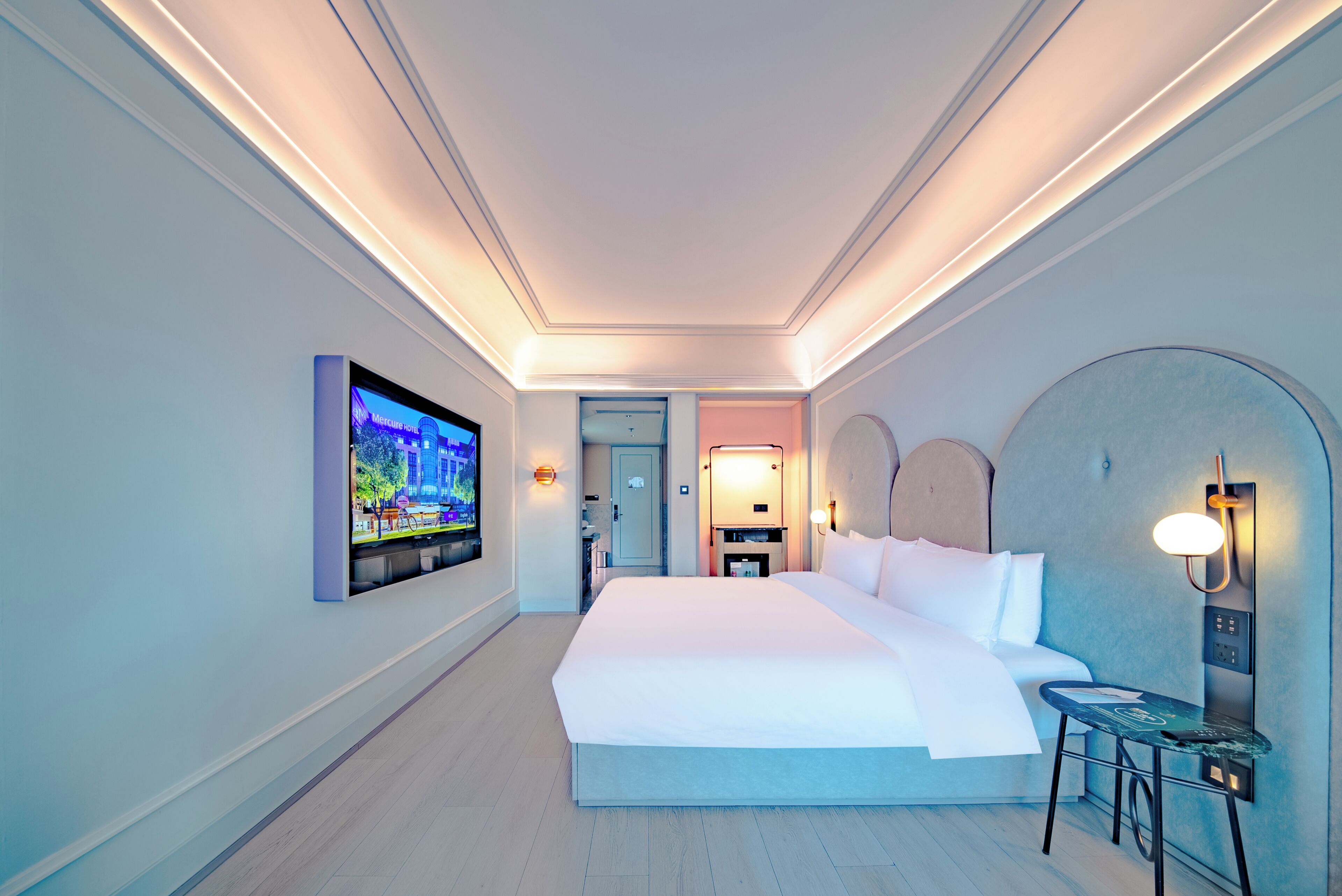 A hotel room with a large bed, a TV mounted on the wall, a desk with a chair, and a small table.