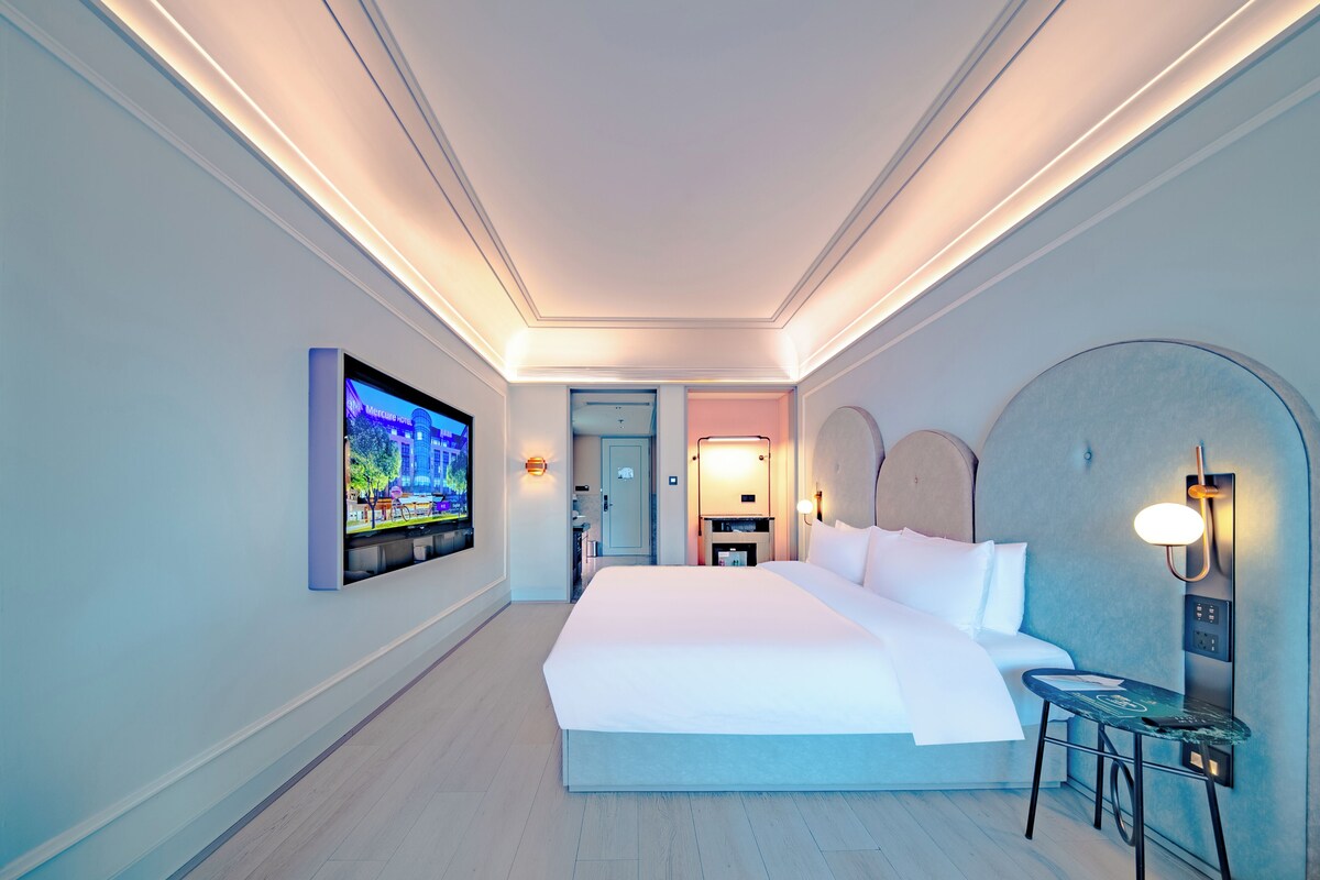 Habitación de hotel con una cama grande, un televisor montado en la pared, un escritorio con una silla y una mesita.