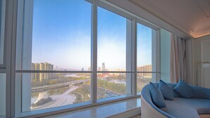Una sala de estar moderna con un ventanal grande, un sofá curvo y vistas a un paisaje urbano y un río.