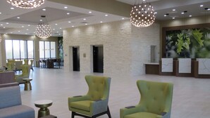 Un vestíbulo espacioso con sillones verdes, un mostrador de recepción y un amplio ventanal que proporciona luz natural.