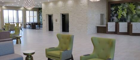 Un hall d’entrée spacieux, doté de fauteuils verts, d’un comptoir de réception et d’une grande fenêtre laissant entrer la lumière naturelle.