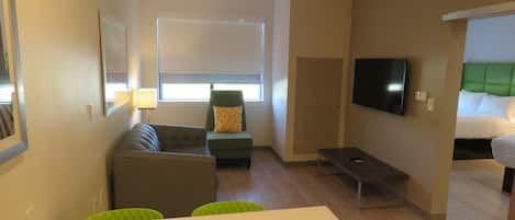 A hotel room with a sofa, a small table, a TV, and a bed with a green headboard.