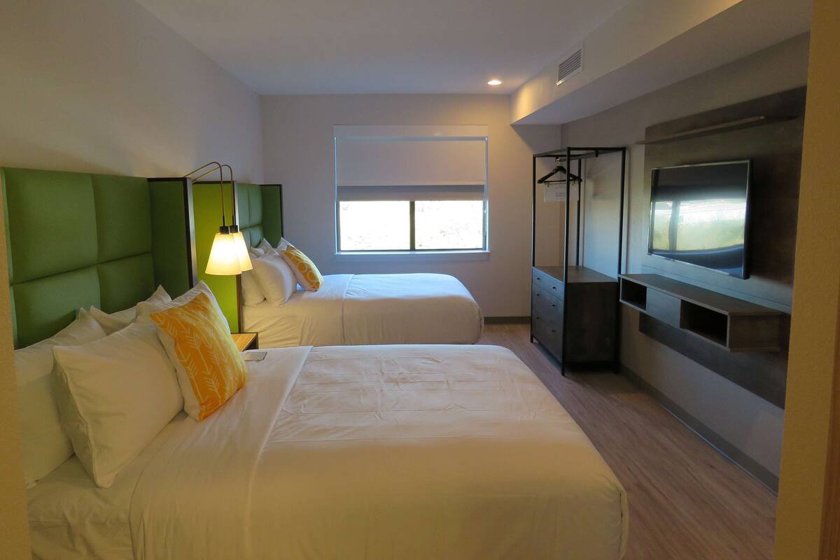 Een hotelkamer met twee bedden, een televisie, een raam en een kledingkast.