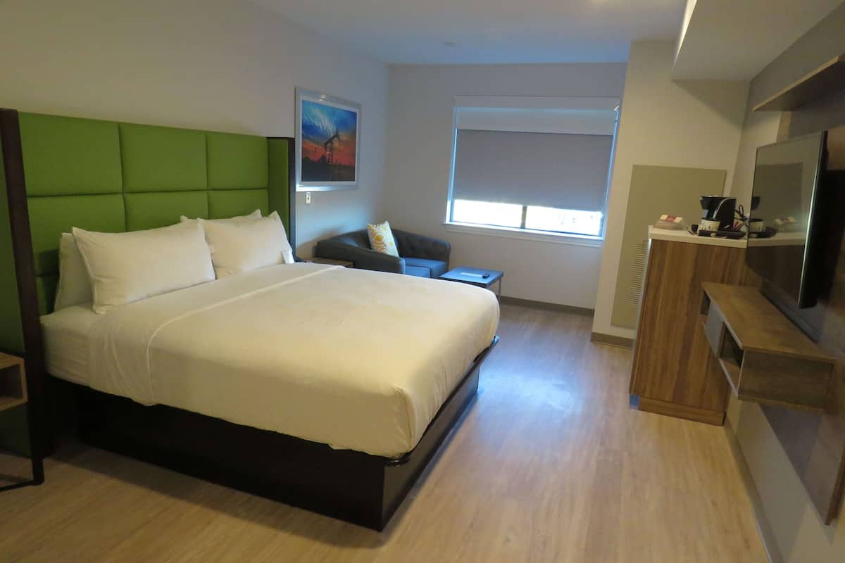 Een moderne hotelkamer met een groot bed, een kleine zithoek, een televisie en een raam met jaloezieën.