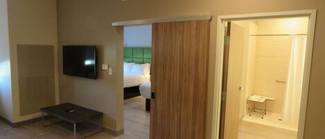 A hotel room with a bed, a TV, a desk, and a bathroom with a shower.