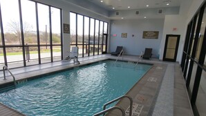 Una piscina interior con ventanas transparentes, una silla de salvavidas y un letrero de advertencia.