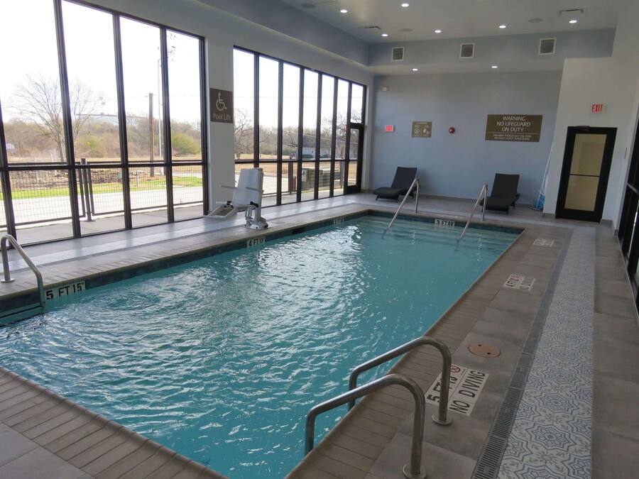 An indoor swimming pool with clear windows, a lifeguard chair, and a warning sign.