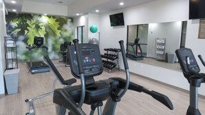Un gimnasio con cintas de correr, elípticas y un espejo grande.