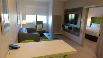 A hotel room with a sofa, a dining table, chairs, a TV, and a bed.