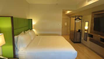Habitación de hotel con una cama grande, una mesita de noche con lámpara, un armario y un televisor en la pared.