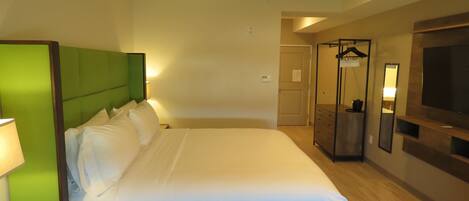 Habitación de hotel con una cama grande, una mesita de noche con lámpara, un armario y un televisor en la pared.