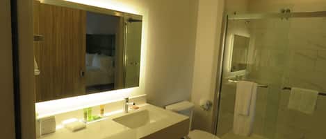 Un baño moderno con un espejo grande, lavamanos, inodoro y ducha con mampara de vidrio.