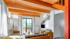Una sala de estar acogedora con vigas de madera, un conjunto de sofás, una mesa de comedor y un televisor montado en la pared.