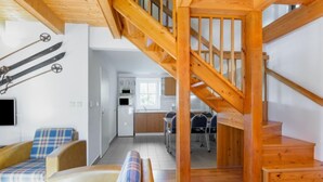 Un interior moderno con una escalera de madera, una zona de cocina y un área de estar con sofá y sillones.