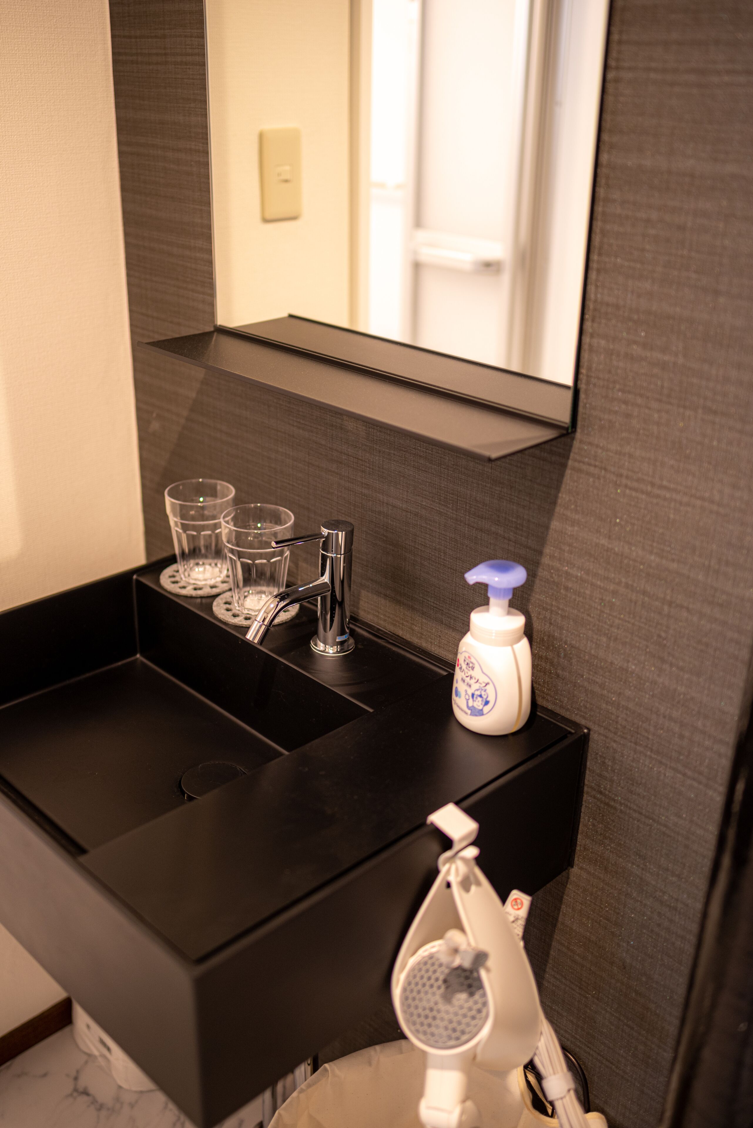 A bathroom sink with a mirror above it, a soap dispenser, and two glasses on the sink's edge.
