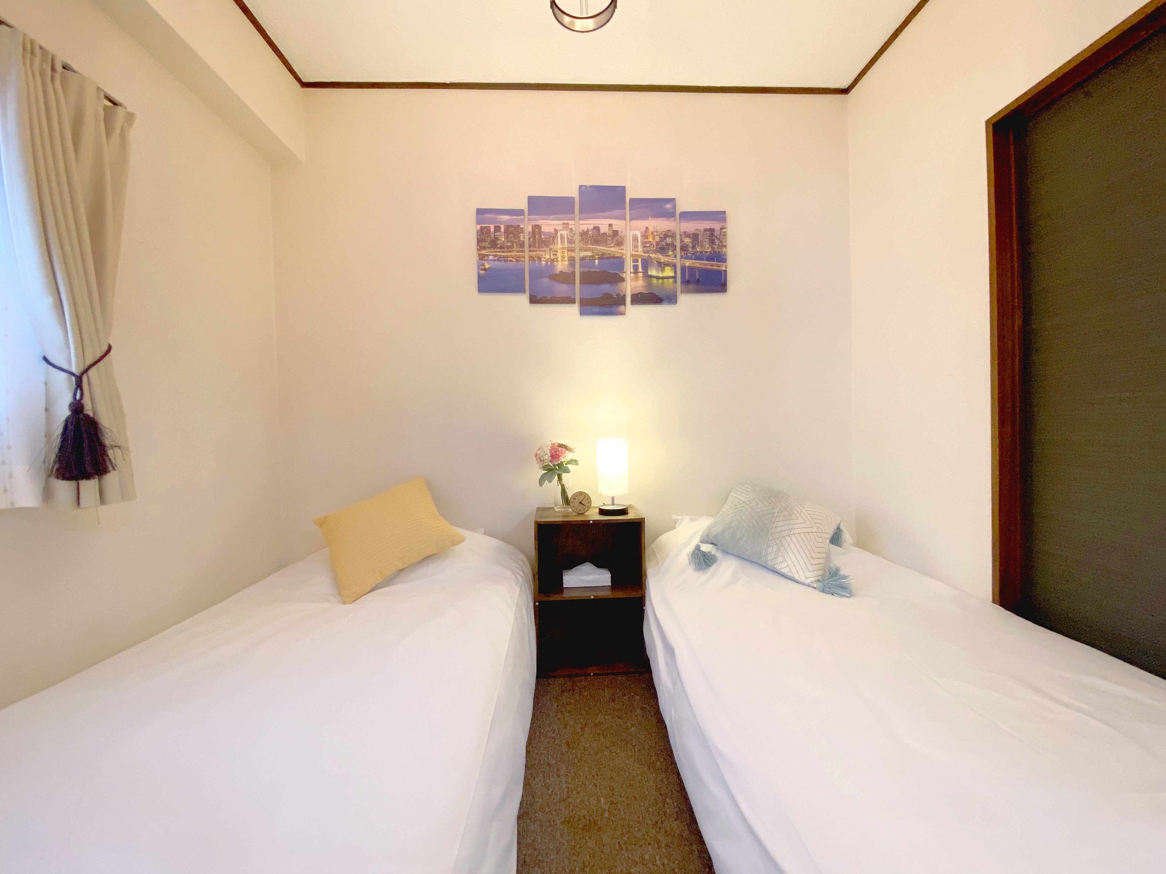 Una camera d'albergo con due letti singoli, un comodino con una lampada e una parete decorata con una composizione di fotografie.