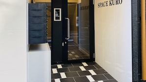 Entrada moderna de un hotel con piso a cuadros blanco y negro, puerta de vidrio y el nombre "SPACE KURO" en la pared.