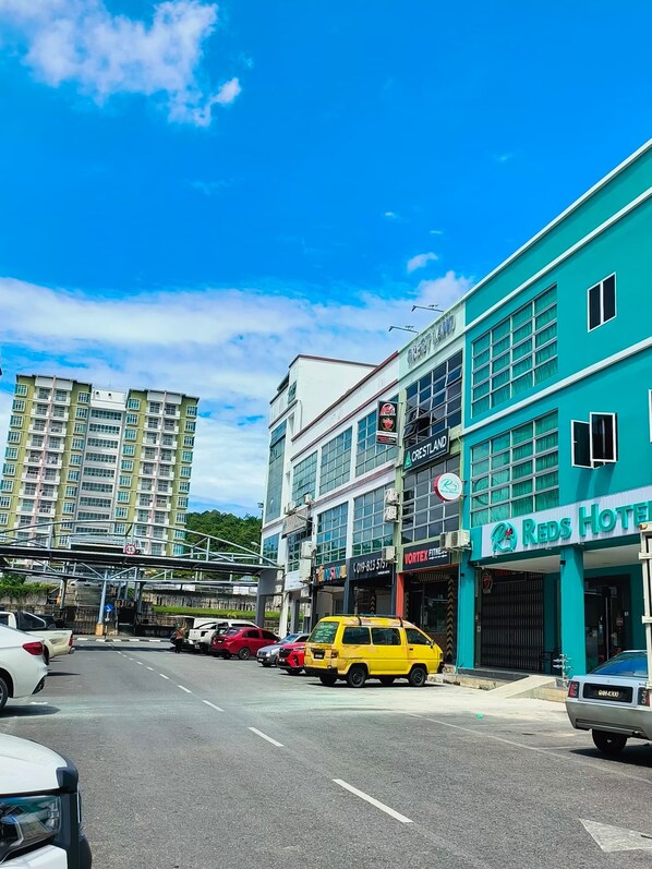 A hotel named 'Reds Hotel' with a signboard, a multi-story building in the background, and a clear sky.